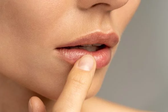 Close up of woman applying moisturizing nourishing balm to her lips with her finger to prevent dryness and chapping in the cold season. Lip protection.